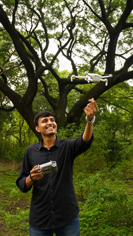 Anshul outdoors holding a controller and reaching upward beneath trees